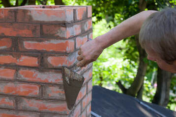 masonry contractor repairing smoothing down a damaged brick chimney